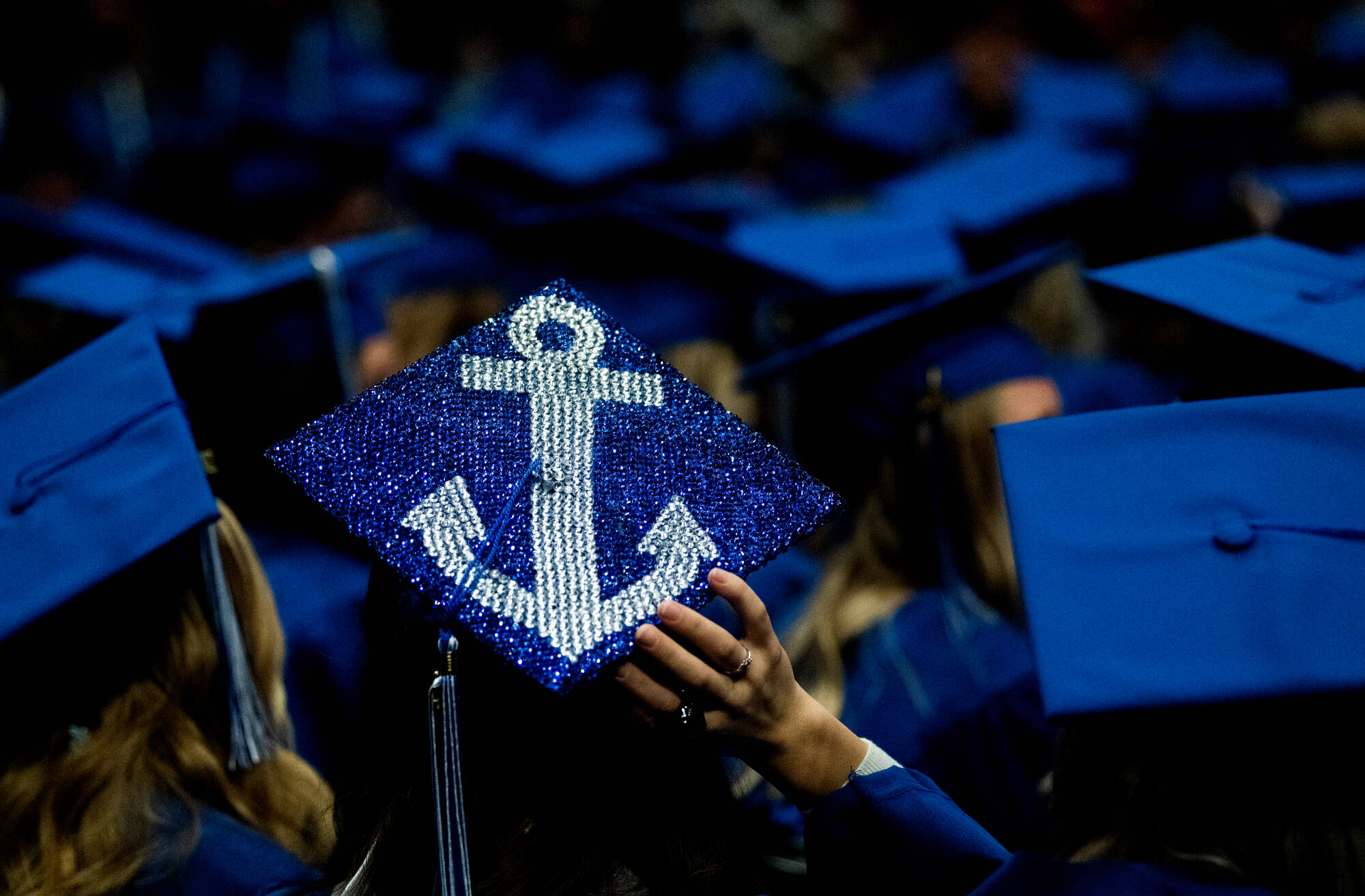 Sea of caps at graduation with one cap decorated with a sequined anchor